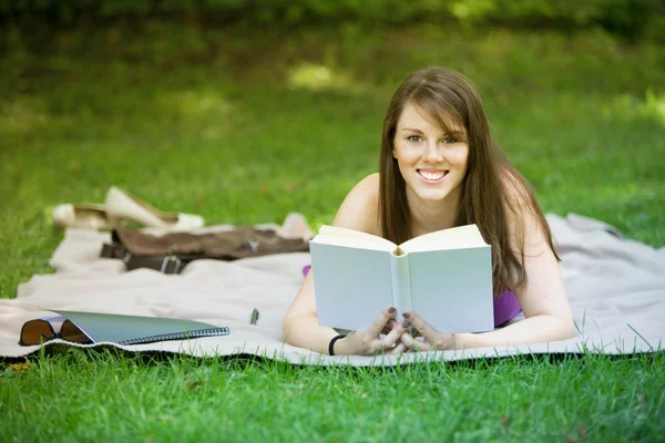 Junge Frau liegt im Park und liest ein Buch — Stockfoto