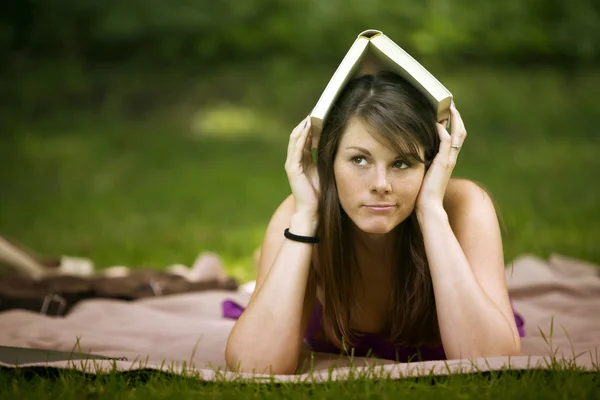 Jovem mulher deitada no parque com livro na cabeça — Fotografia de Stock