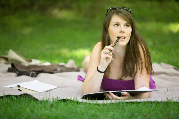 Jovem mulher deitada no parque e estudando — Fotografia de Stock