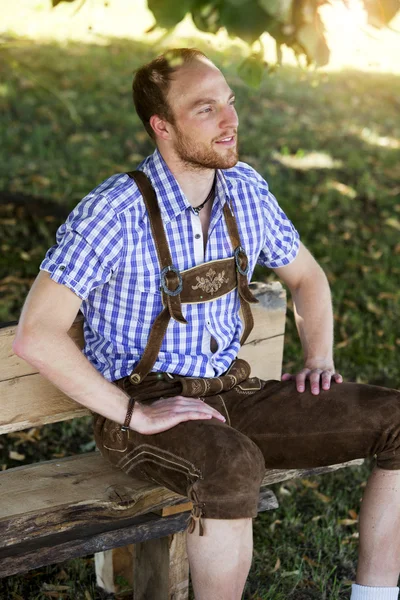Jovem em roupas tradicionais da Baviera sentado no banco — Fotografia de Stock