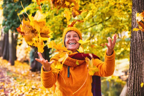 Szczęśliwa Kobieta Pięćdziesiątce Zewnątrz Jesienią Bawi Się Spadającymi Liśćmi — Zdjęcie stockowe