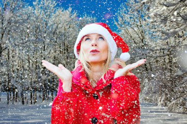 Karlı bir ormanda Noel Baba gibi giyinmiş sarışın bir kadın.