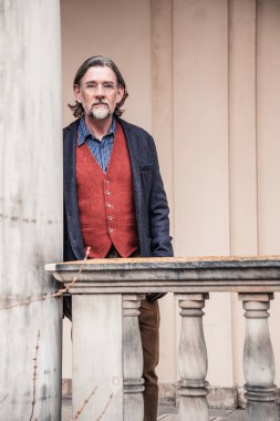 Dışarıda binanın önünde duran 50 'li yaşlarda yakışıklı bir adamın portresi.