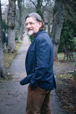 50 'li yaşlarda yakışıklı bir adamın parkta yürürken portresi.