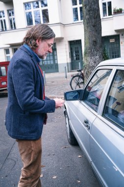 50 'li yaşlarda yakışıklı bir adam elinde anahtarla arabasının yanında duruyor.