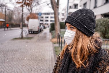 Genç esmer kadın, açık havada, karlı bir günde, maske takıyor.