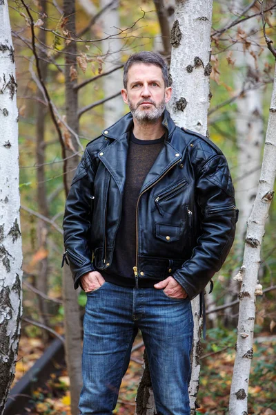 handsome man in leather jacket and jeans standing in forest