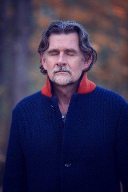 50 'lerinde, gözleri kapalı, sakallı yakışıklı bir adamın portresi.