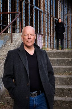 Terk edilmiş binada duran bir adamın portresi ve hemen arkasında bir kadın.