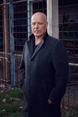 50 'li yaşlarda, siyah ceketli yakışıklı bir adam abadnoned Buidling' de dikiliyor.