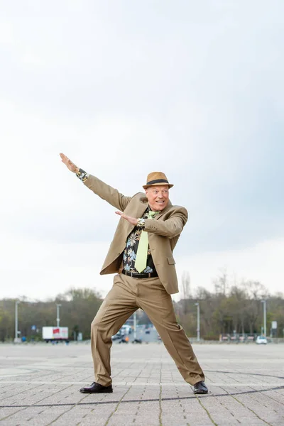 man in his 50s in a brown suit from the 1980s dancing on the street