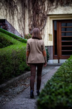 Binaya doğru yürüyen takım elbiseli esmer bir kadının arkası.