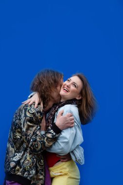 Genç ve havalı bir çift mavi bir arka planda sarılıp gülüyor.