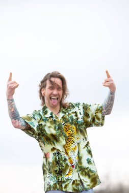 Uzun saçlı, bağıran ve el işareti yapan yakışıklı genç adamın portresi.