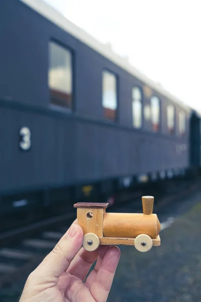 close-up of hand holding toy train in front of historic big train