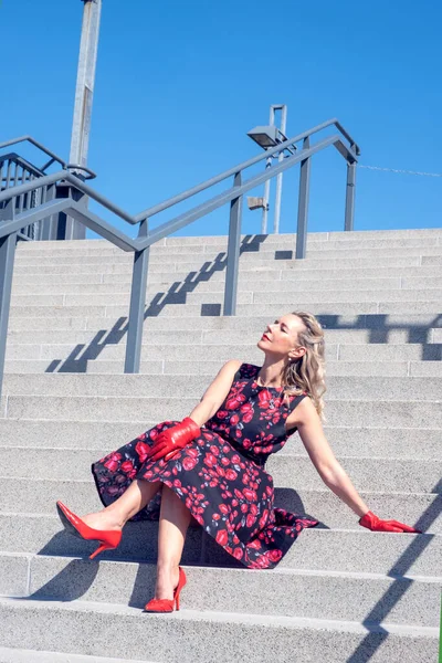 ブロンド女性です赤いドレス階段に座って太陽を楽しんで — ストック写真