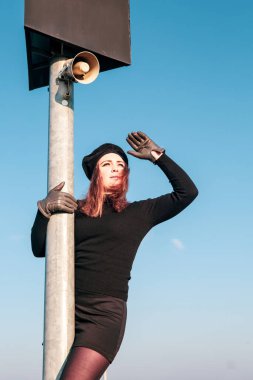 Siyah balıkçı yakalı genç esmer kadın hoparlörle direkte dikiliyor ve uzaklığa bakıyor.