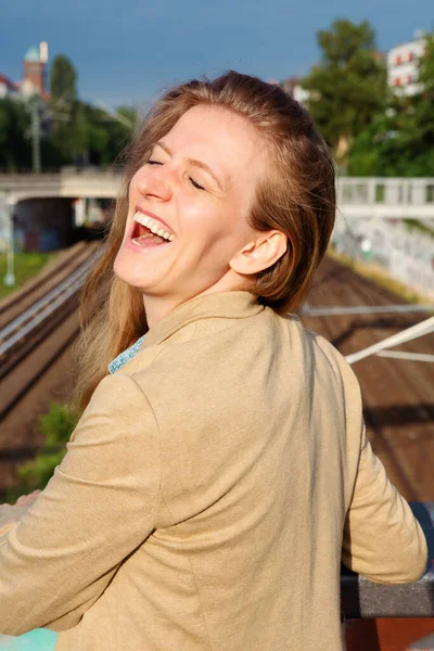 鉄道の近くに立って笑っている美しい金髪の若い女性の肖像画 — ストック写真