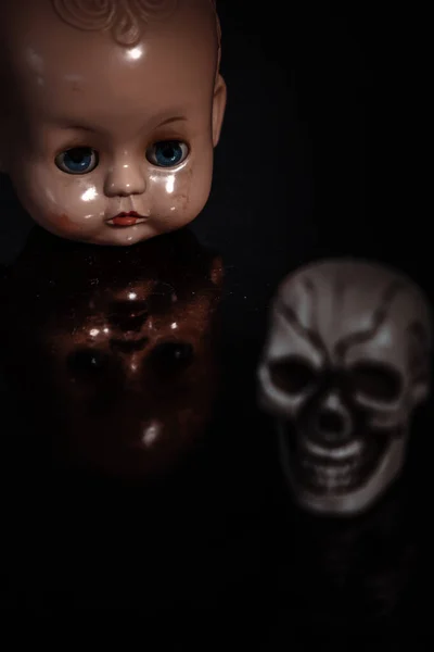 close-up of an old doll head with reflection and a skull