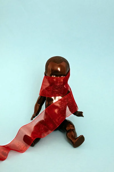 Black Doll Covered Red Ribbon Sitting Blue Background — Stock Photo, Image