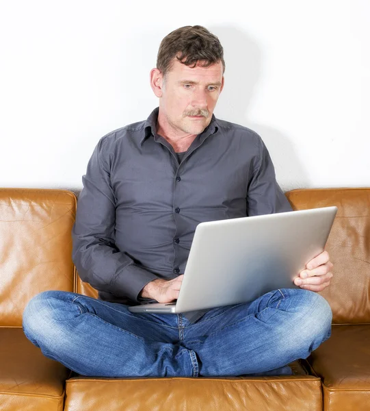 男子坐在沙发上用的笔记本电脑 — 图库照片