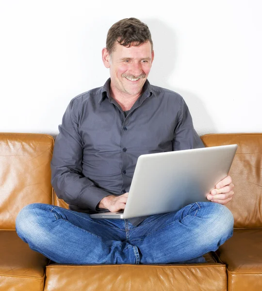 Człowiek siedzi na kanapie z laptopem — Zdjęcie stockowe