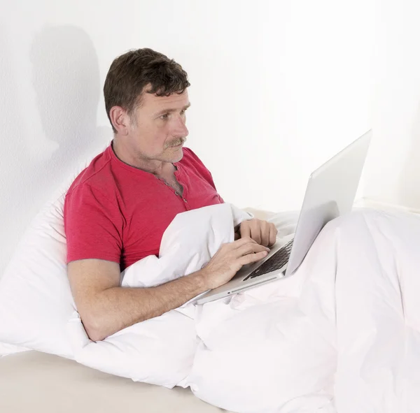 Человек в постели с ноутбуком — стоковое фото