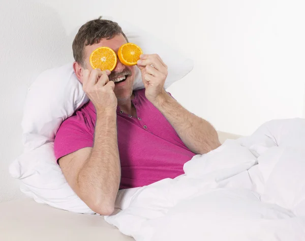 Homem na cama com laranjas — Fotografia de Stock