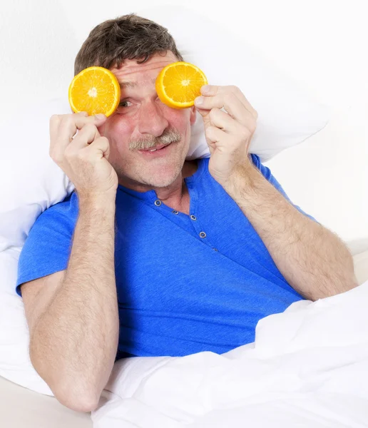 Homem na cama com laranjas — Fotografia de Stock