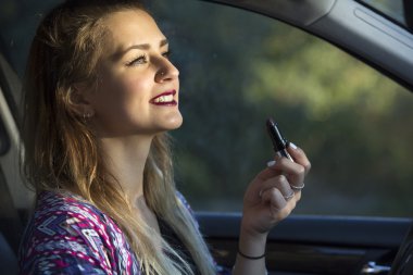 Kadın arabada ruj sürüyor.