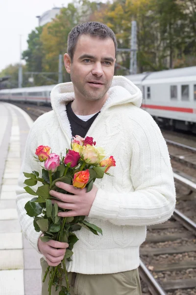 Hombre esperando en la estación de tren con flores —  Fotos de Stock