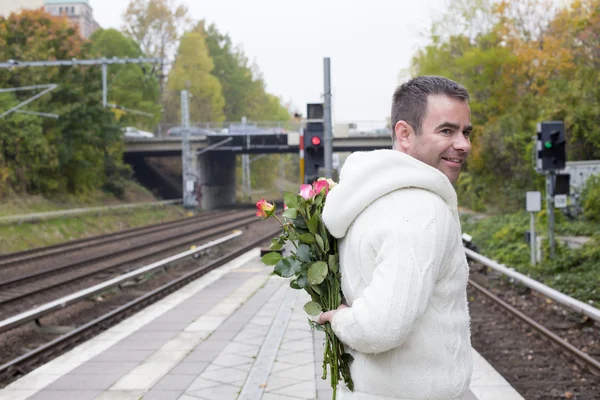 Homem esperando na estação de trem com flores — Fotografia de Stock