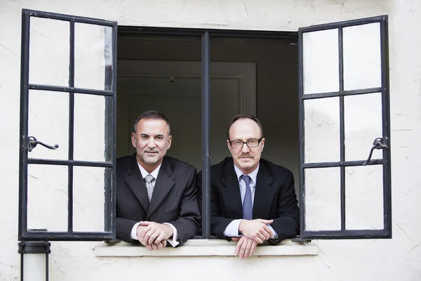 Dos hombres de negocios mirando por una ventana — Foto de Stock