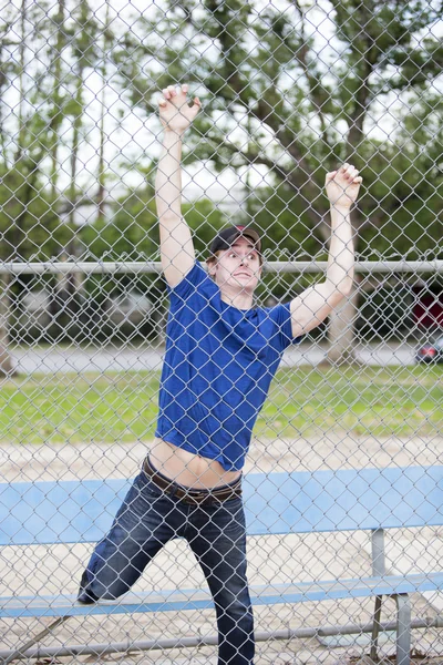 Młody człowiek wisi na ogrodzenie w sportsfield — Zdjęcie stockowe