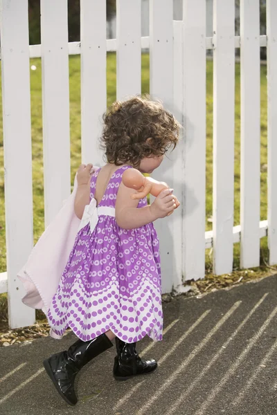 Onun bebek ile beyaz çit önünde küçük kız — Stok fotoğraf