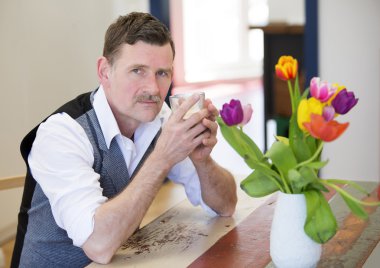 onun elinde bir glas ile masada oturan adam