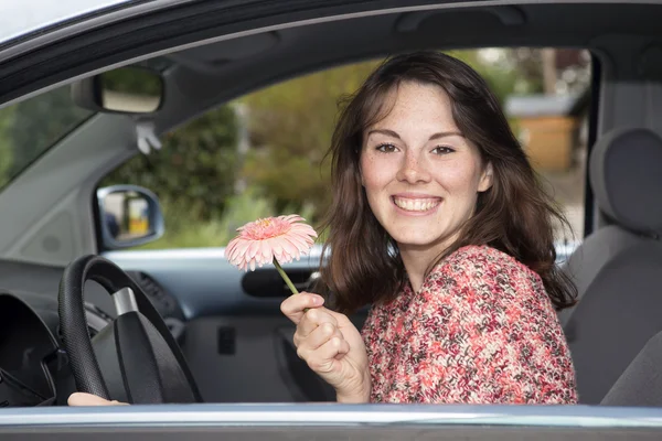 Jeune femme assise dans une voiture et tenant une fleur — Photo