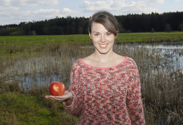 Young woman holding an apple in her hand outdoors — Stock Photo, Image