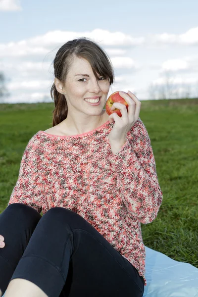 Young woman sitting outdoors holding an apple — Stock Photo, Image