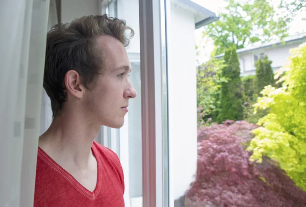 Jeune homme blond regardant par la fenêtre — Photo