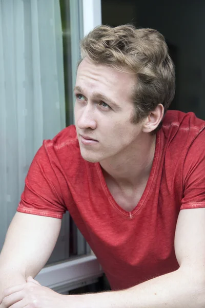 Young blond man looking out of window — Stock Photo, Image