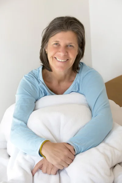 Mujer sonriente sentada en la cama — Foto de Stock