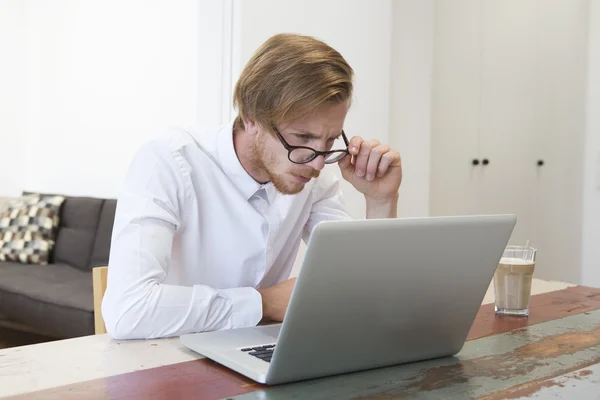 Ung man sitter vid hem tittar på sin laptop — Stockfoto