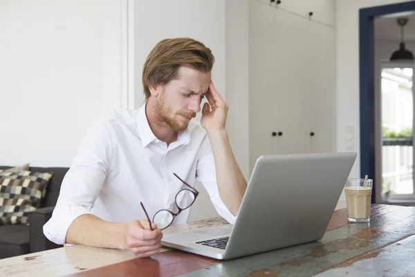 Dizüstü bilgisayar ve bir baş ağrısı ile oturan genç adam — Stok fotoğraf