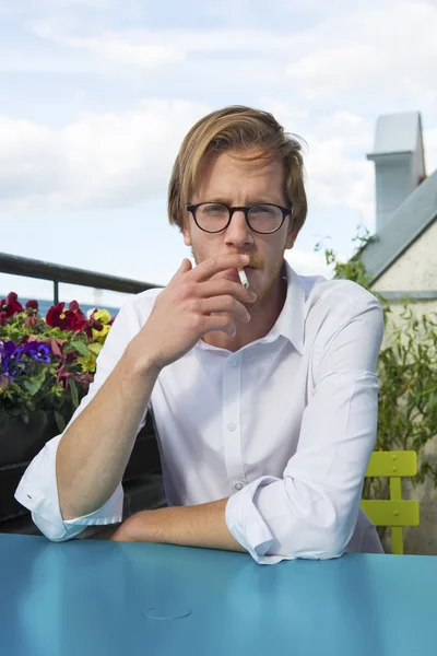 Mladý muž sedí na balkóně a kouření cigaret — Stock fotografie