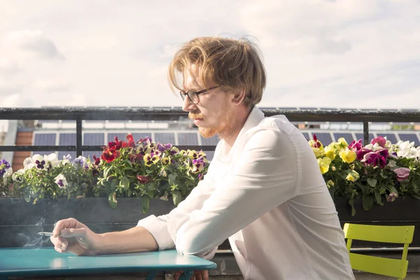 Jonge man zittend op balkon en het roken van een sigaret — Stockfoto