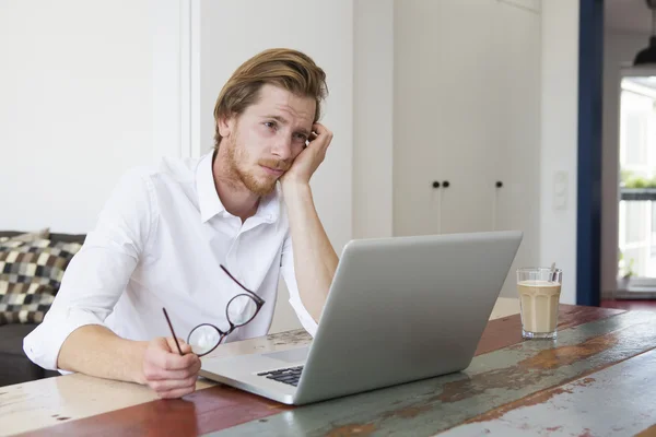 Jonge man zitten met laptop en op zoek triest Stockafbeelding