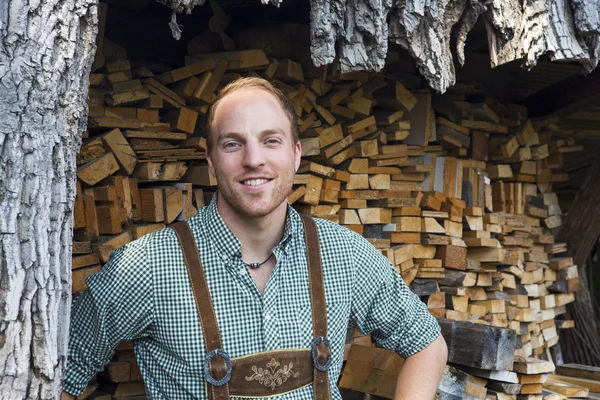 Joven en Lederhosen frente a la leña —  Fotos de Stock