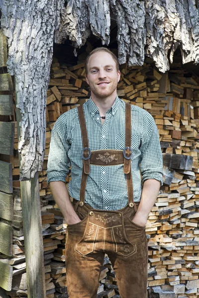 Joven en bavarian lederhosen delante de la leña — Foto de Stock