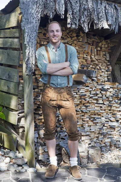 Young man in bavarian lederhosen in front of firewood — Stock Photo, Image